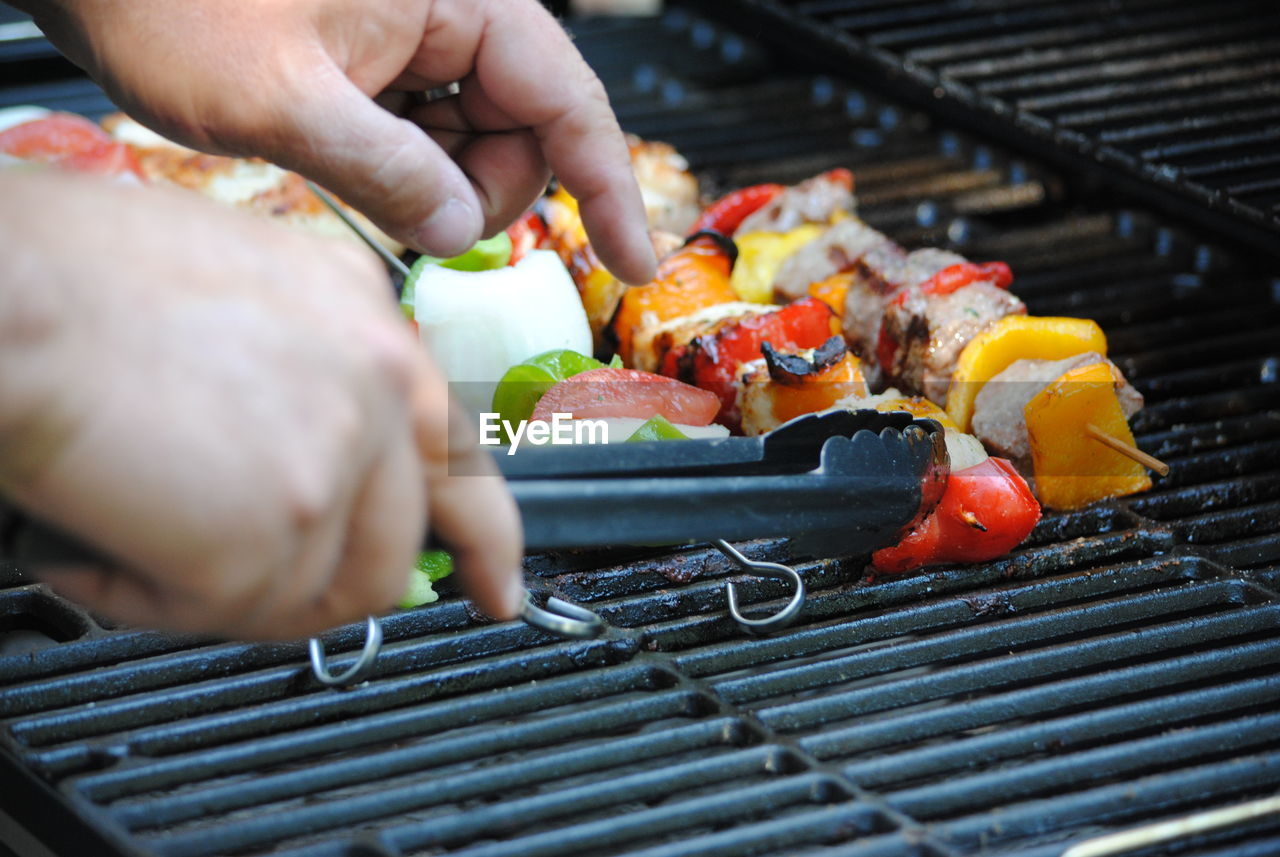 Cropped hand holding serving tongs by food in skewers on barbecue grill