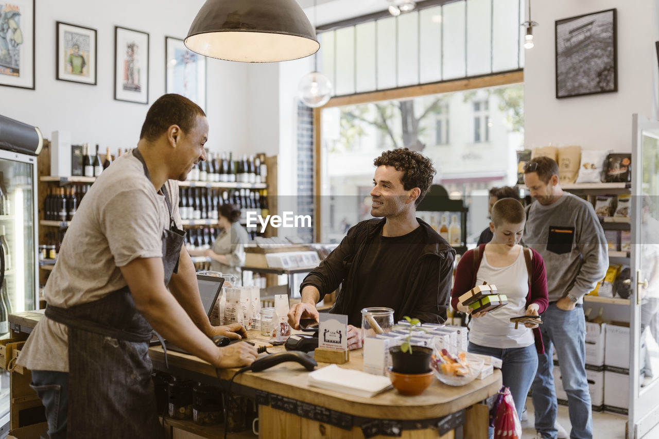 Male owner talking with customer at checkout counter in store