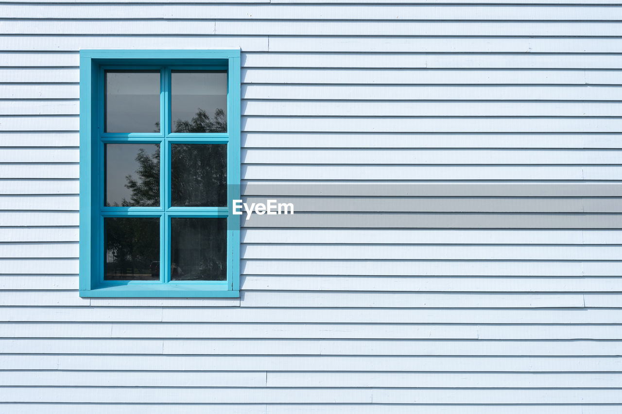 Side of a clapboard building with a window, painted blue.