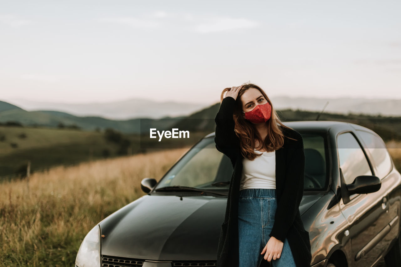 Woman standing by car on field against sky