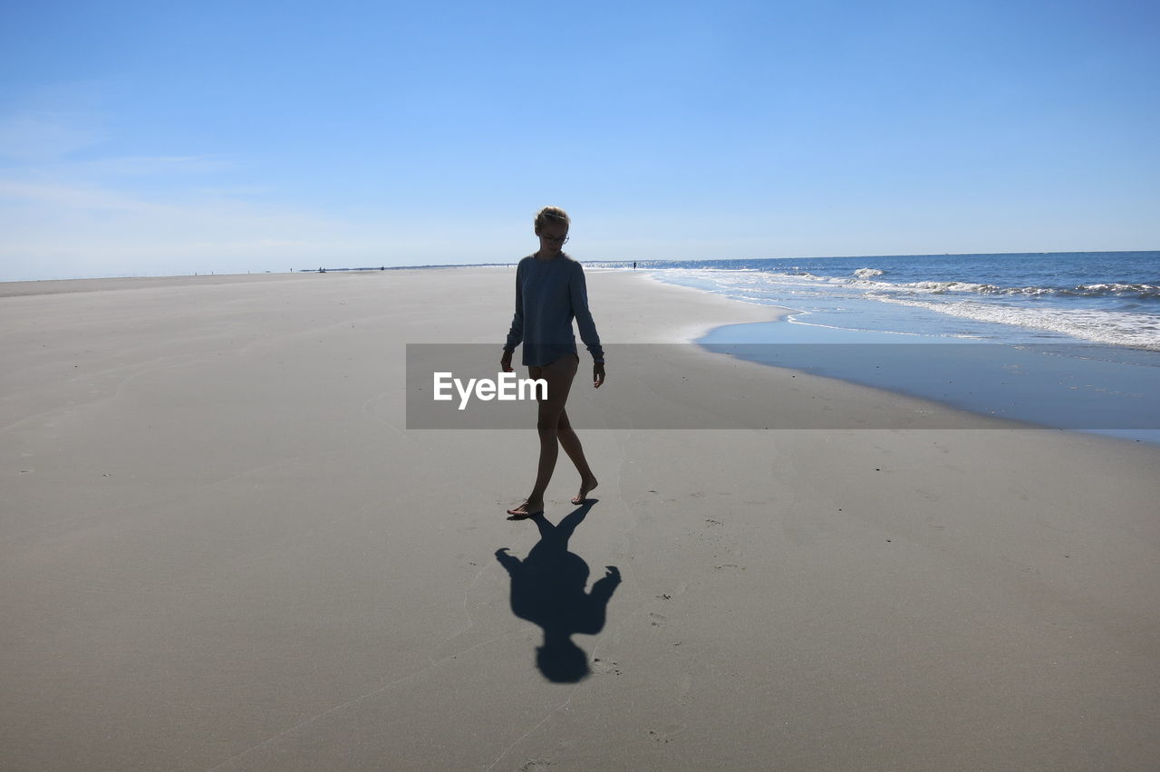 Full length of woman walking at beach against sky during sunny day