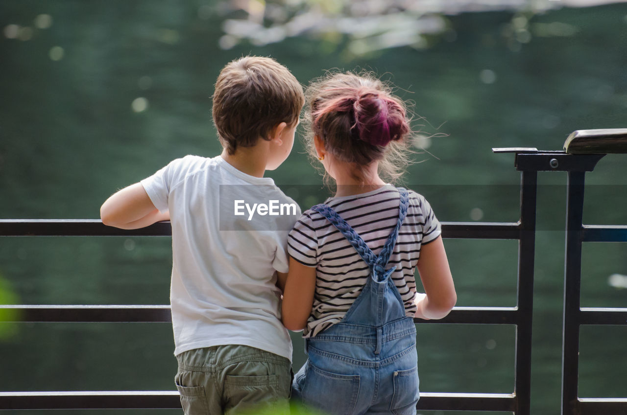 Rear view of siblings standing by railing against lake