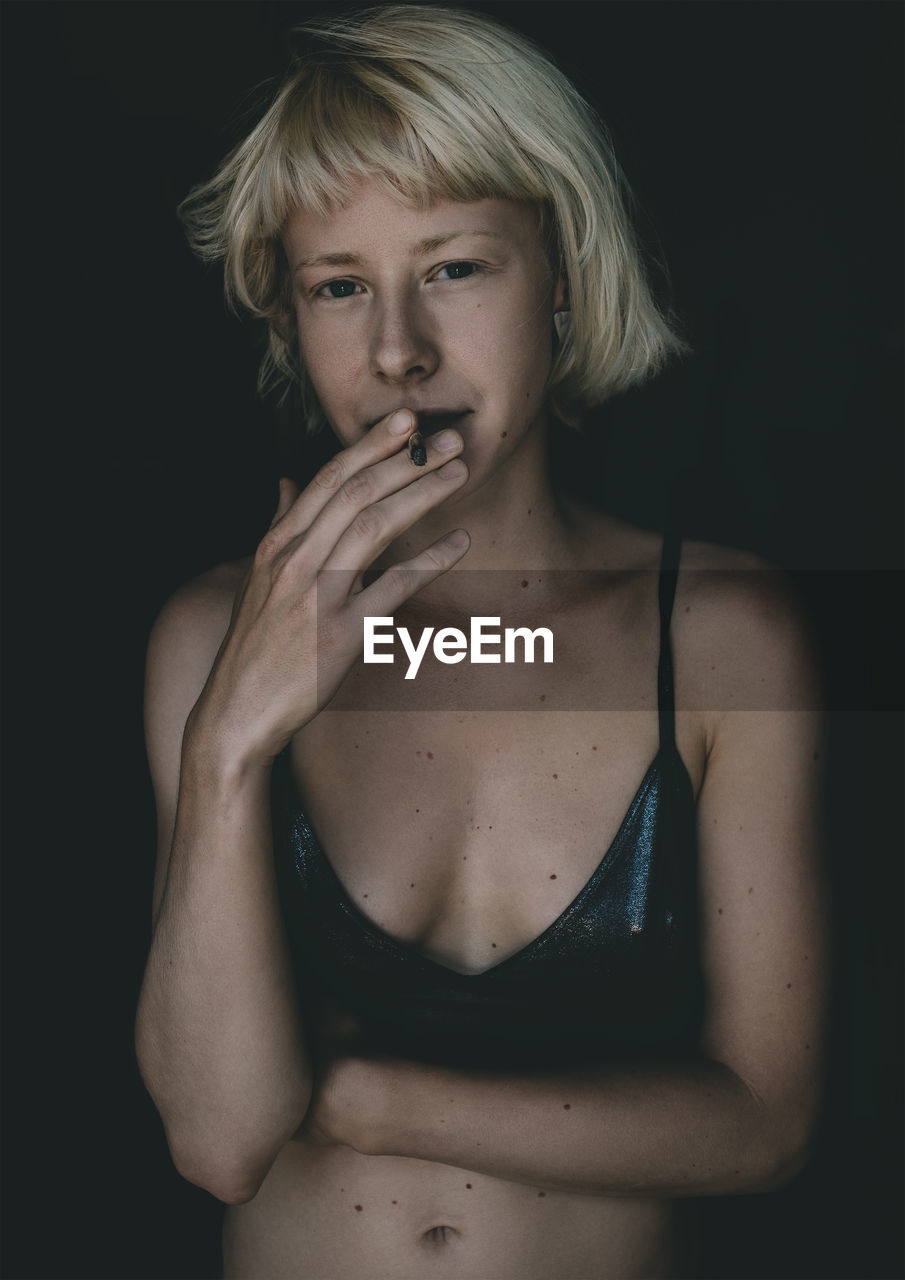 Portrait of young woman smoking against black background