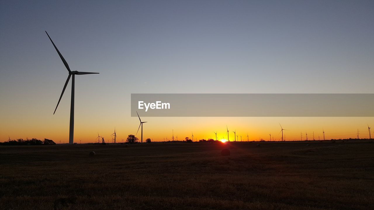 Windmills on field against clear sky during sunset