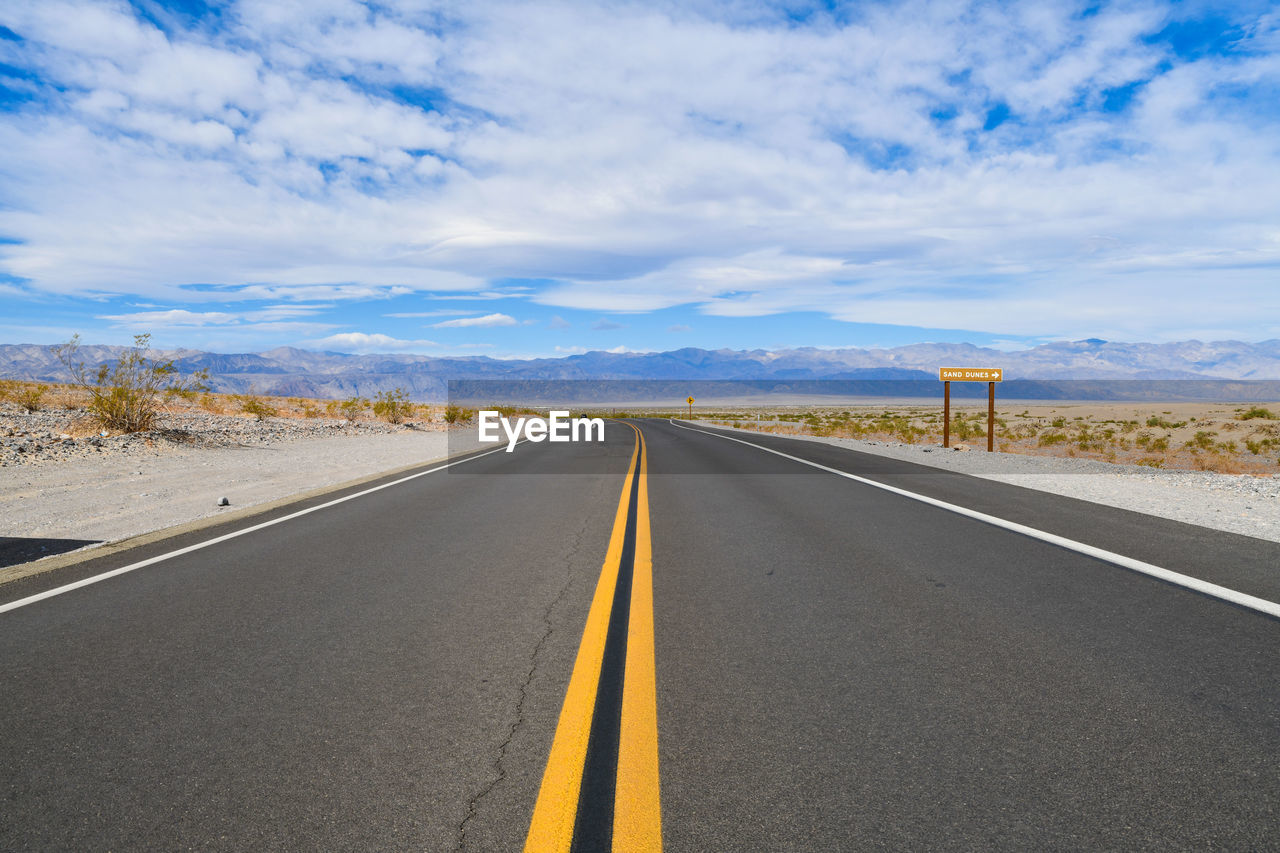 Road passing through landscape against cloudy sky