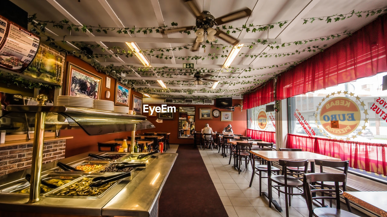 EMPTY CHAIRS AND TABLES IN ILLUMINATED RESTAURANT