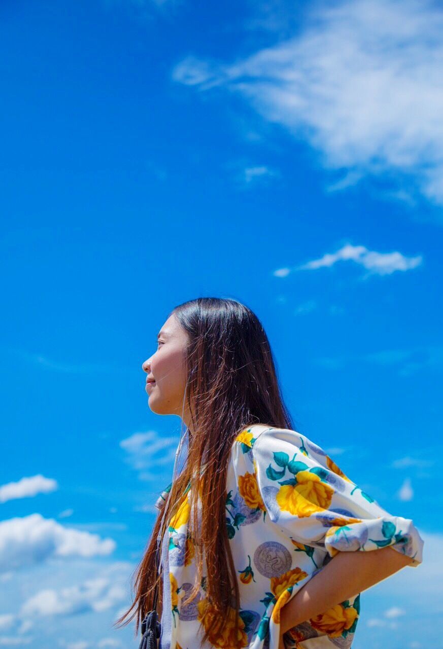 Side view of smiling woman standing against cloudy sky