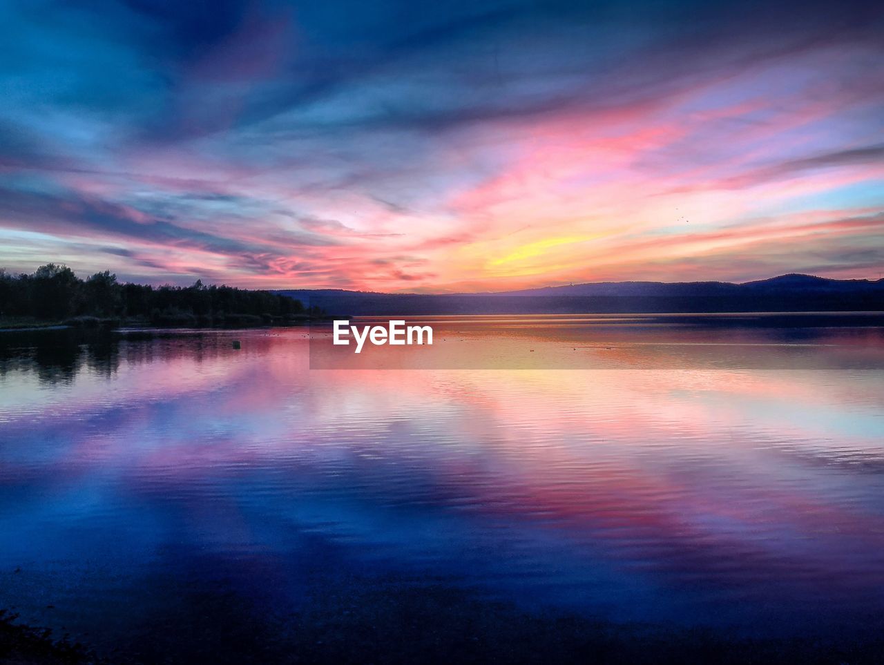 Scenic view of lake against dramatic sky during sunset