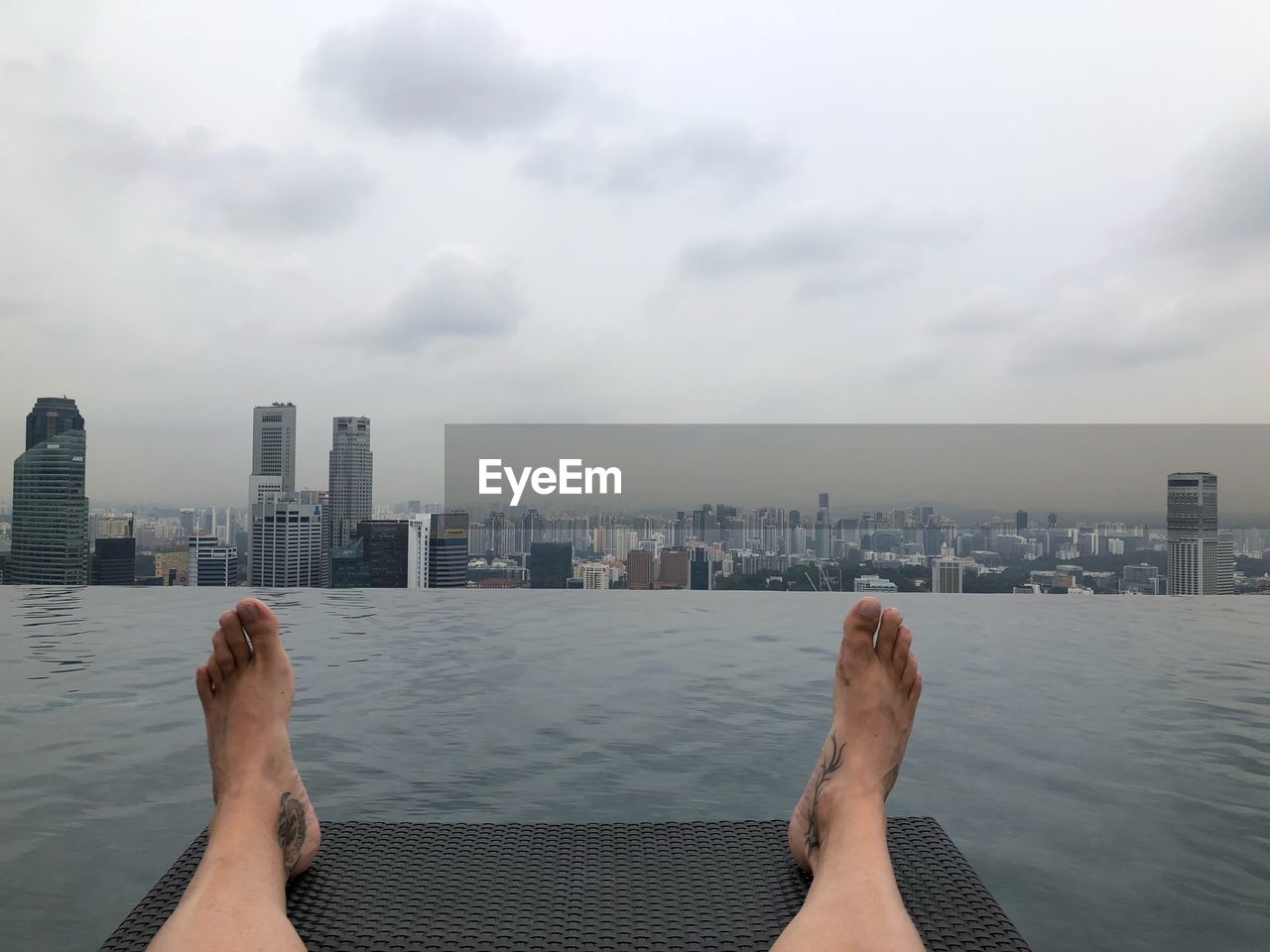 Low section of man on pier over river against cityscape