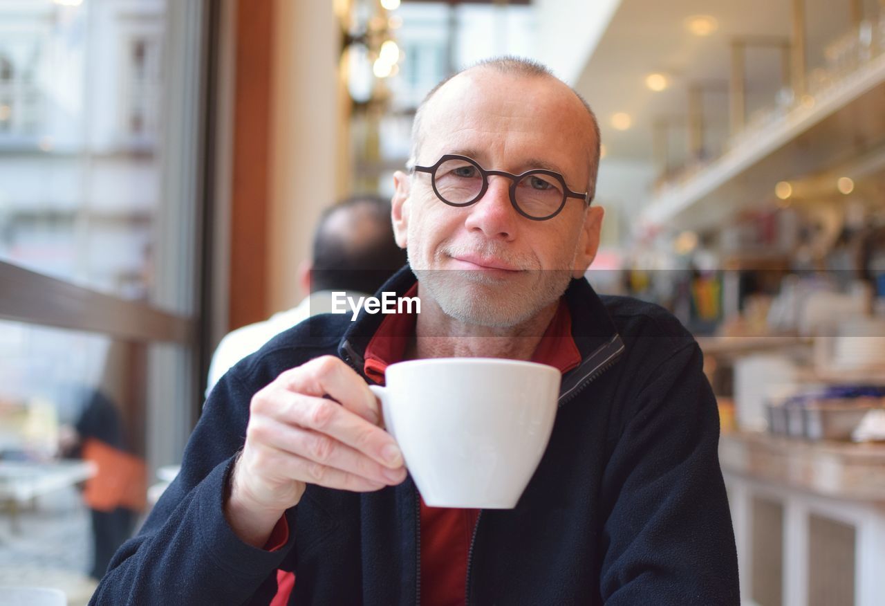 Portrait of mature man drinking coffee while sitting by window in cafe