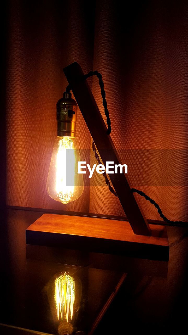 Close-up of illuminated electric lamp on table against curtain in room