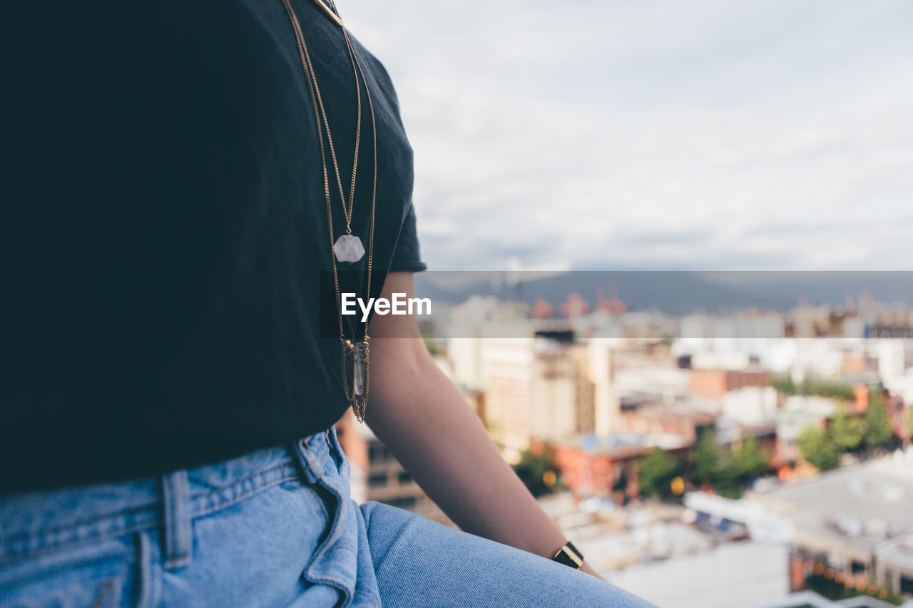 Midsection of woman in city against cloudy sky