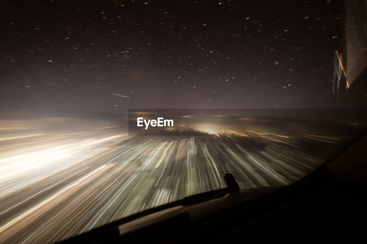 LIGHT TRAILS IN SKY SEEN THROUGH CAR WINDSHIELD AT NIGHT