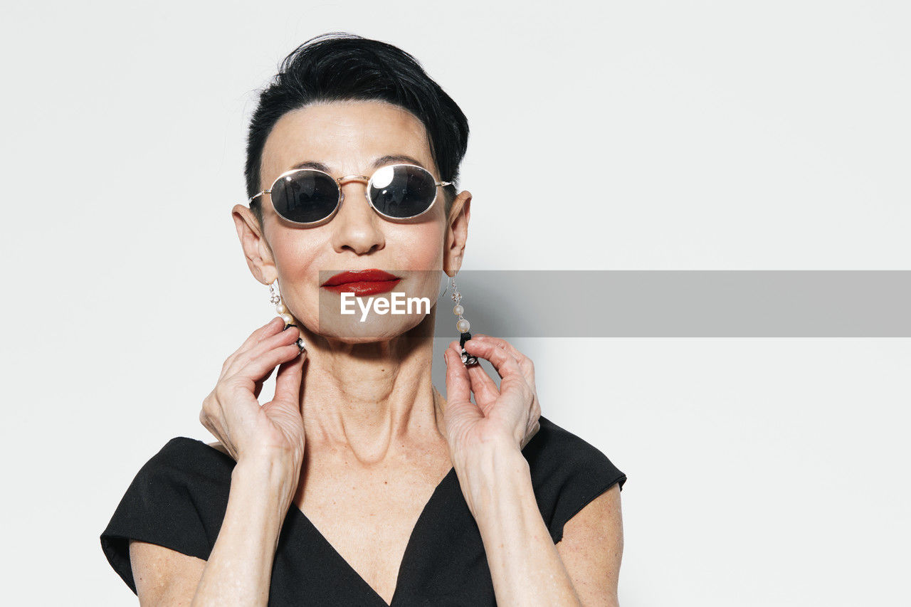 portrait of young woman wearing sunglasses while standing against white background