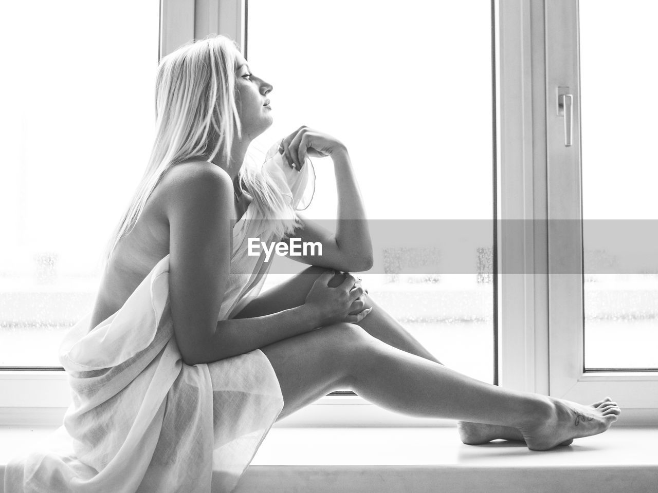 Sensuous woman wrapped in fabric sitting on window sill