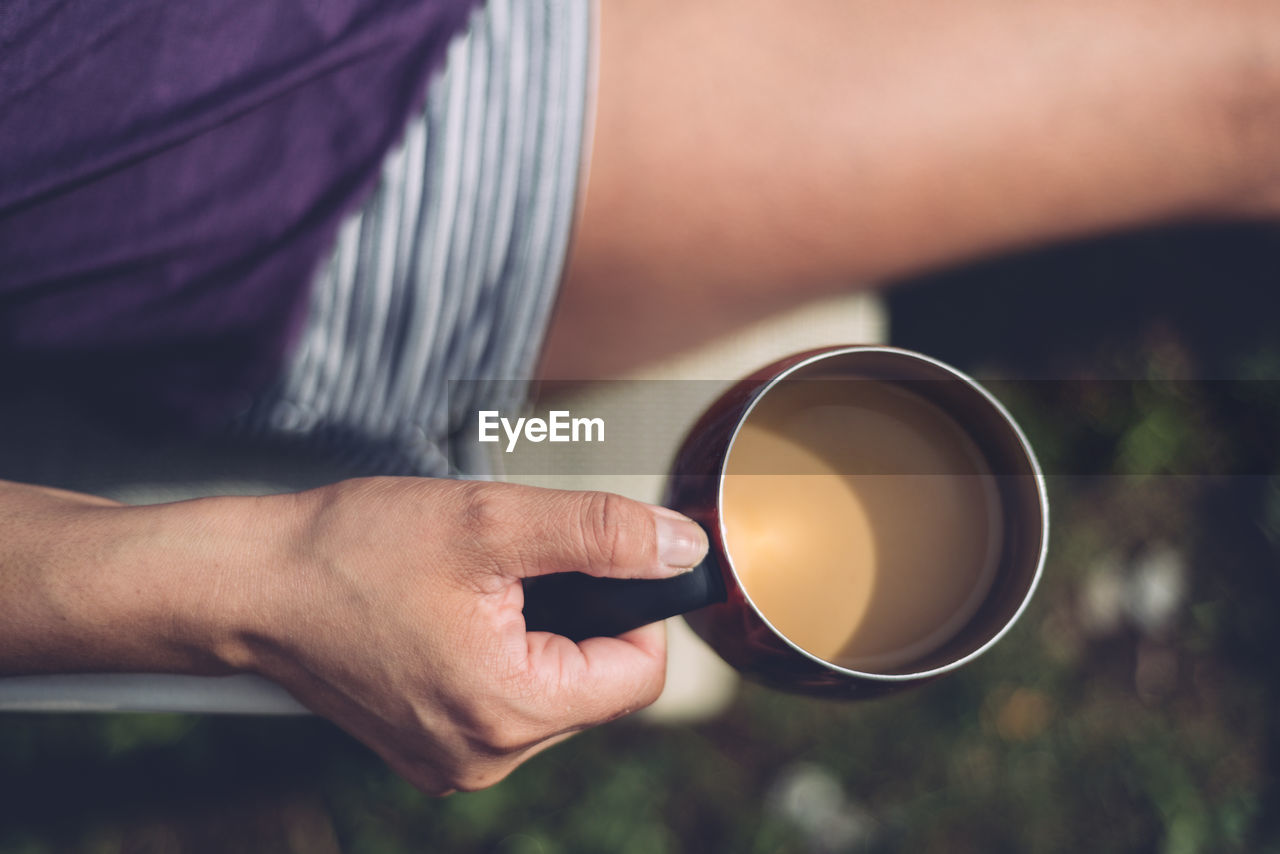 Midsection of woman having tea while sitting outdoors