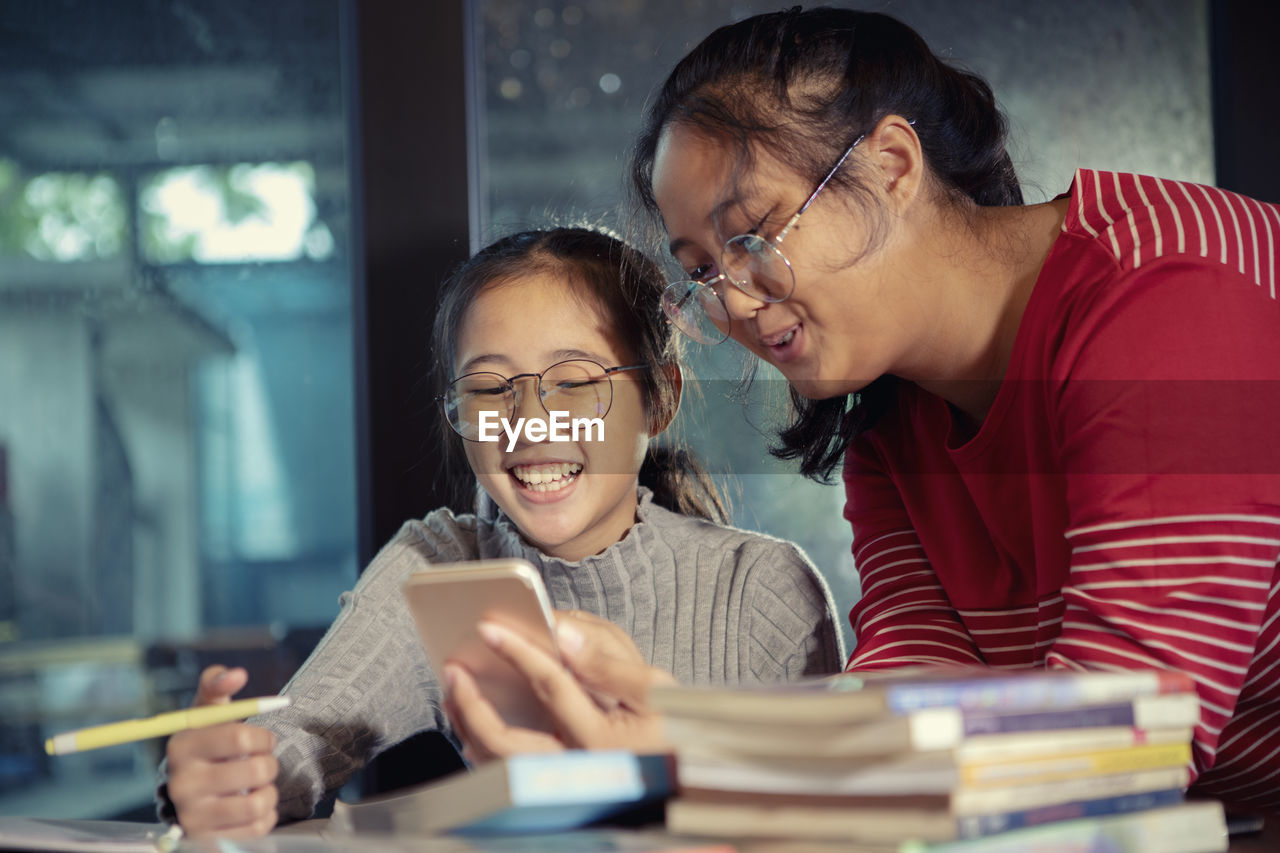 Smiling girls looking at smart phone in library