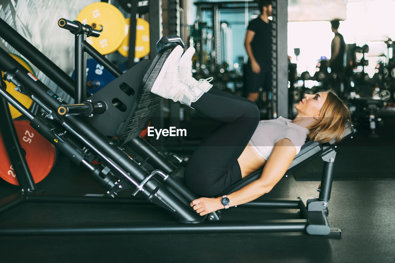 A young woman does exercises for her legs and buttocks while lying on a modern simulator in the gym