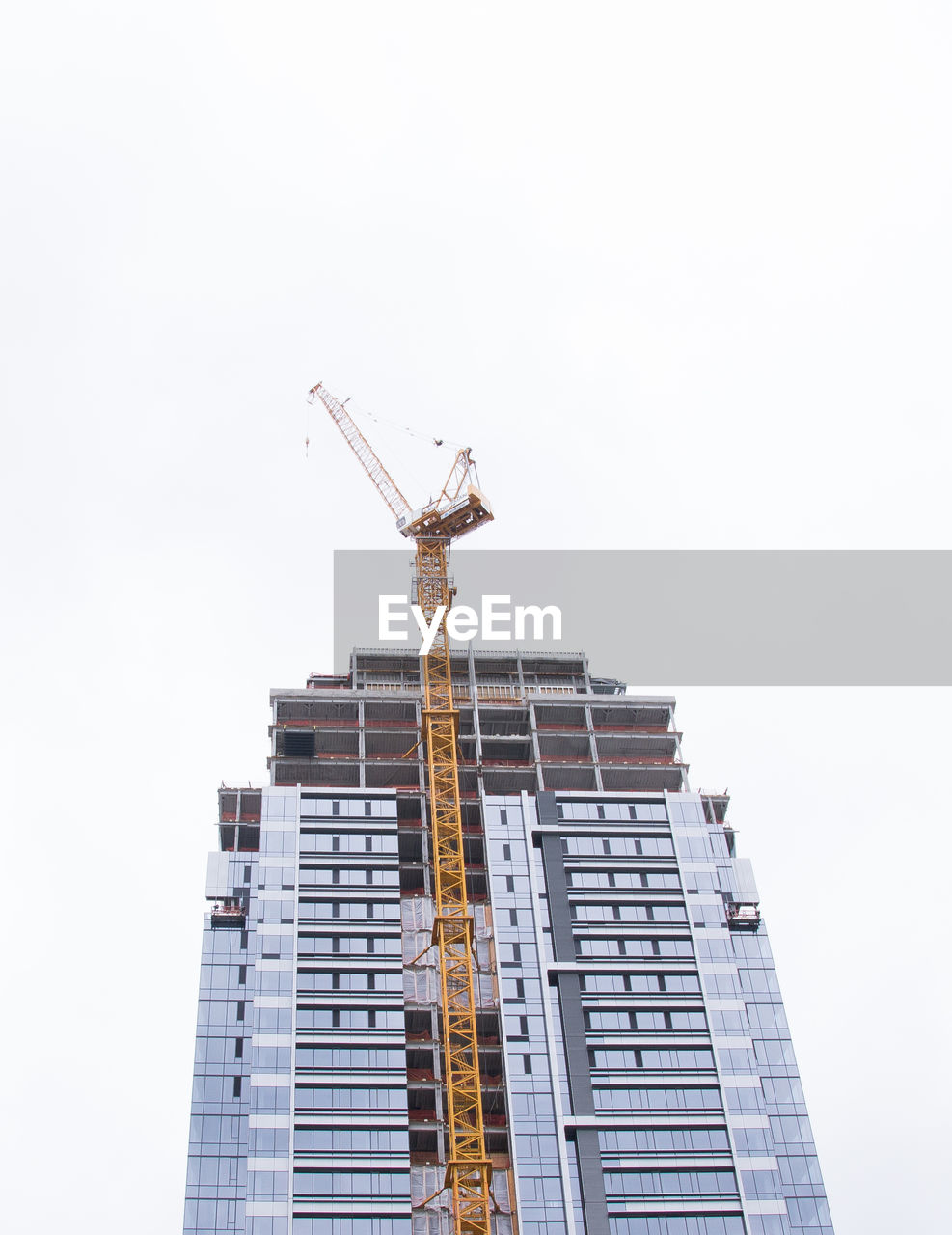 Low angle view of crane next to building against overcast sky