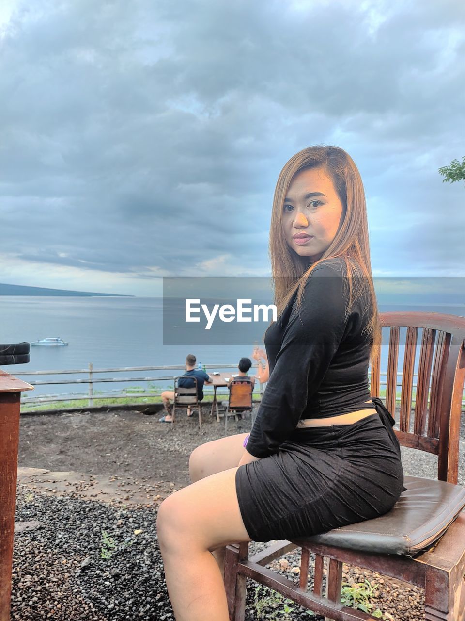 YOUNG WOMAN SITTING BY RAILING AGAINST SEA