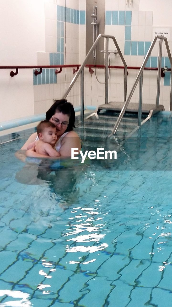 Mother carrying baby boy in swimming pool