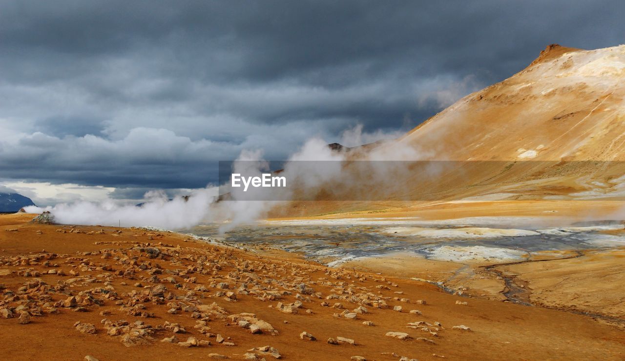 Scenic view of steam over hot springs against cloudy sky