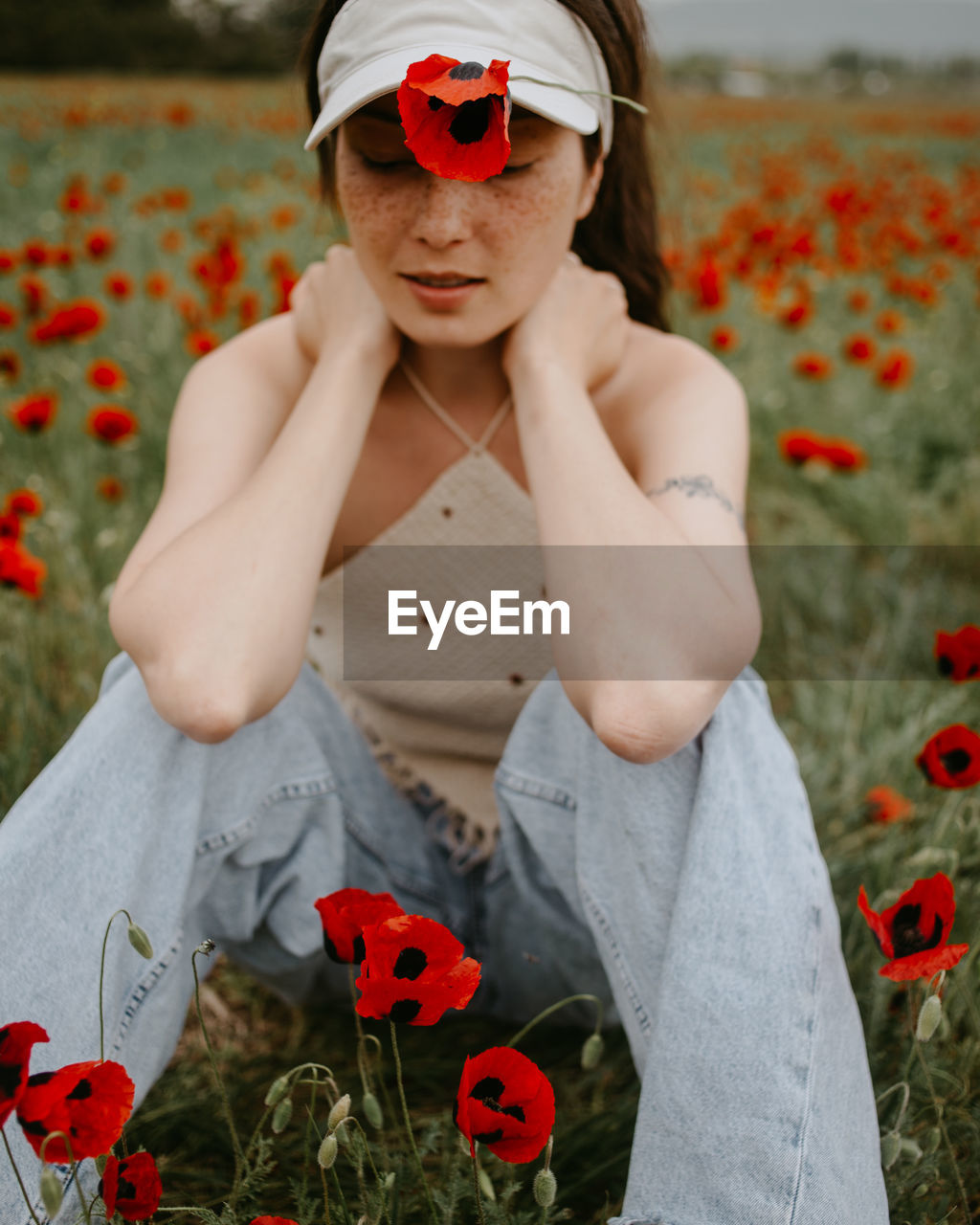 Attractive young woman sitting in the poppy field with flowers