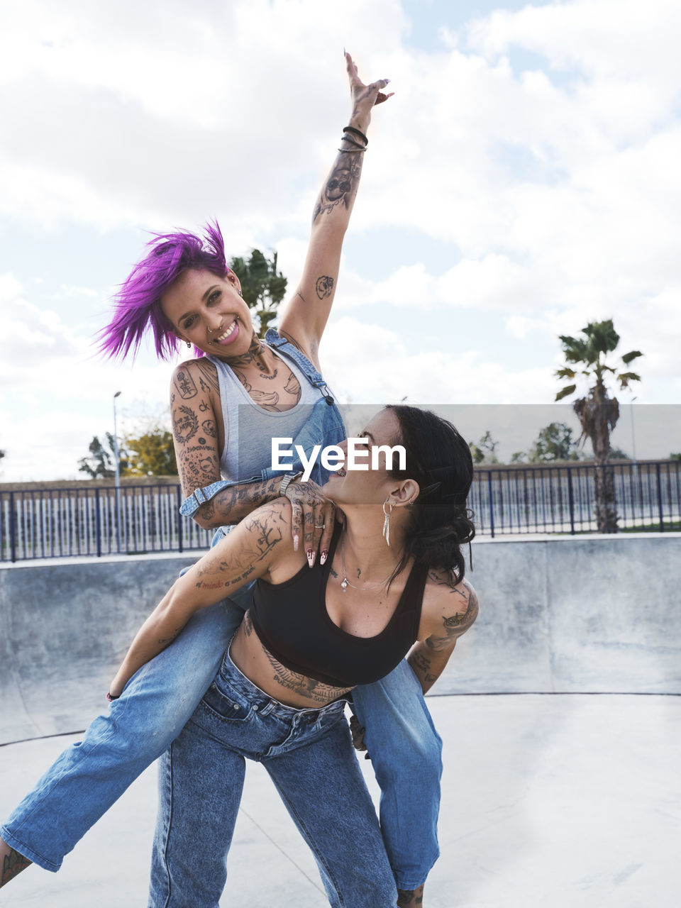 Low angle of delighted woman with pink hair piggybacking cheerful female friend with tattoos while having fun together at weekend