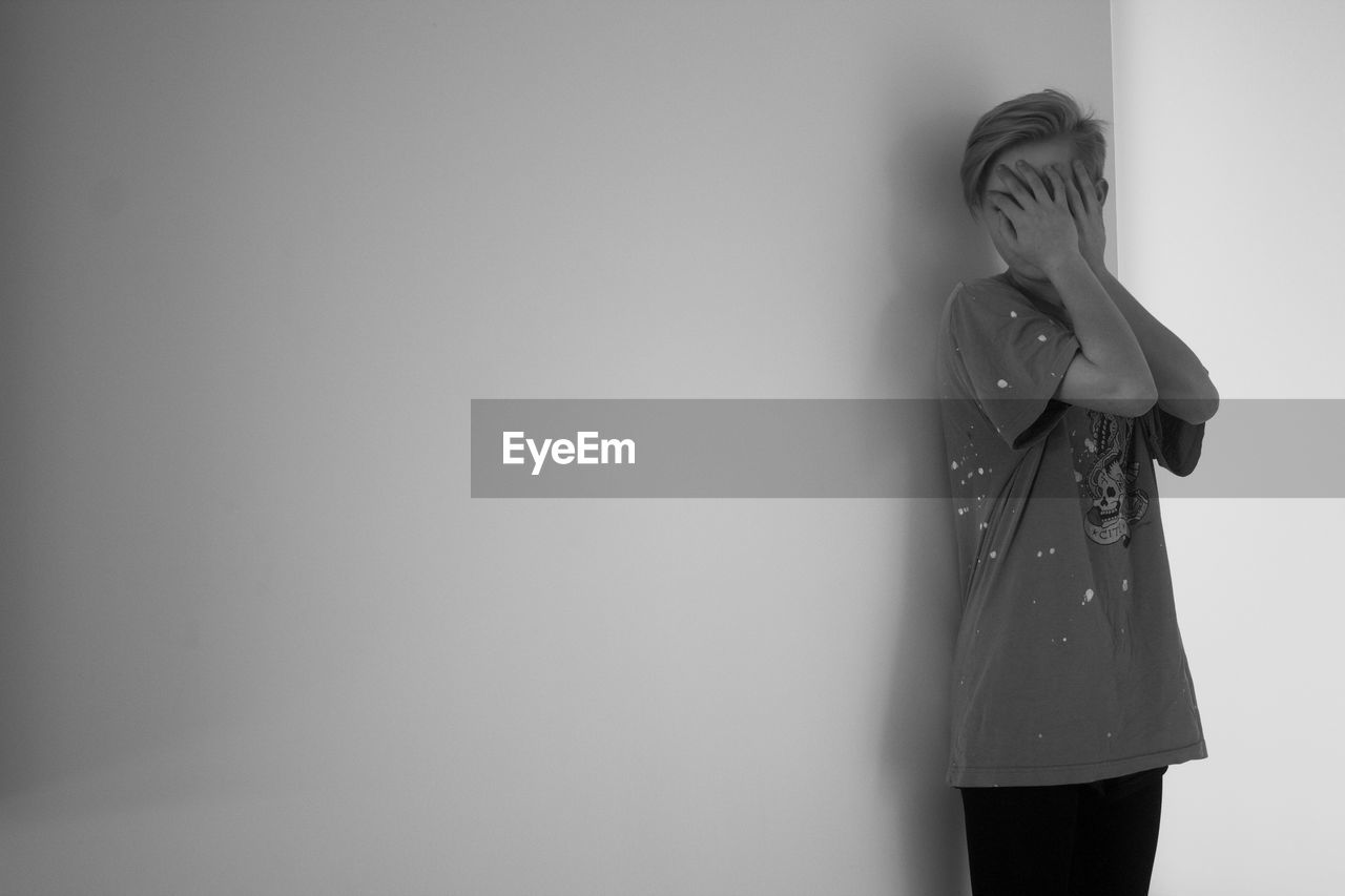 Young woman covering face while standing against wall