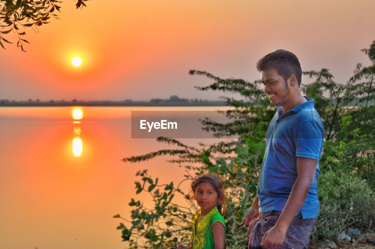 Young man standing in lake against sky during sunset