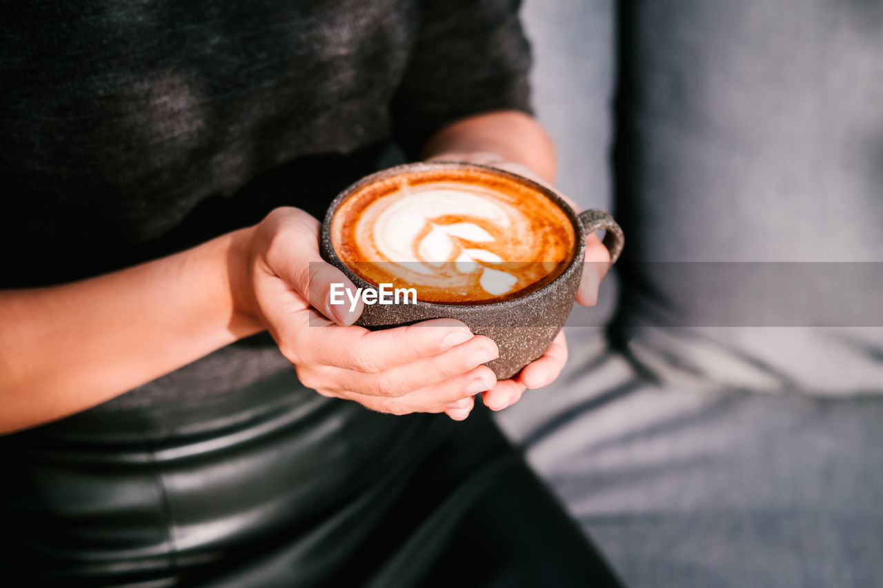 Woman in a black clothing holds coffee in a grey ceramic cup. latte art coffee cup.