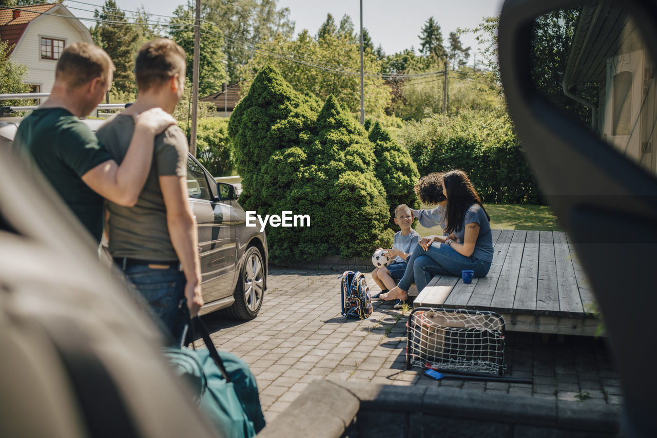 Lesbian mothers looking at son while gay couple standing by car during sunny day