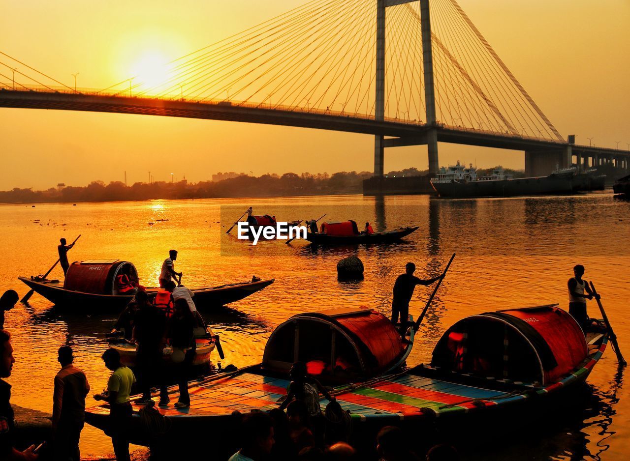 transportation, water, sunset, nautical vessel, sky, bridge, mode of transportation, architecture, nature, evening, built structure, travel destinations, boat, travel, sea, silhouette, dusk, city, vehicle, orange color, sun, tourism, suspension bridge, sunlight, beauty in nature, outdoors, group of people, reflection, twilight, scenics - nature, tranquility, moored