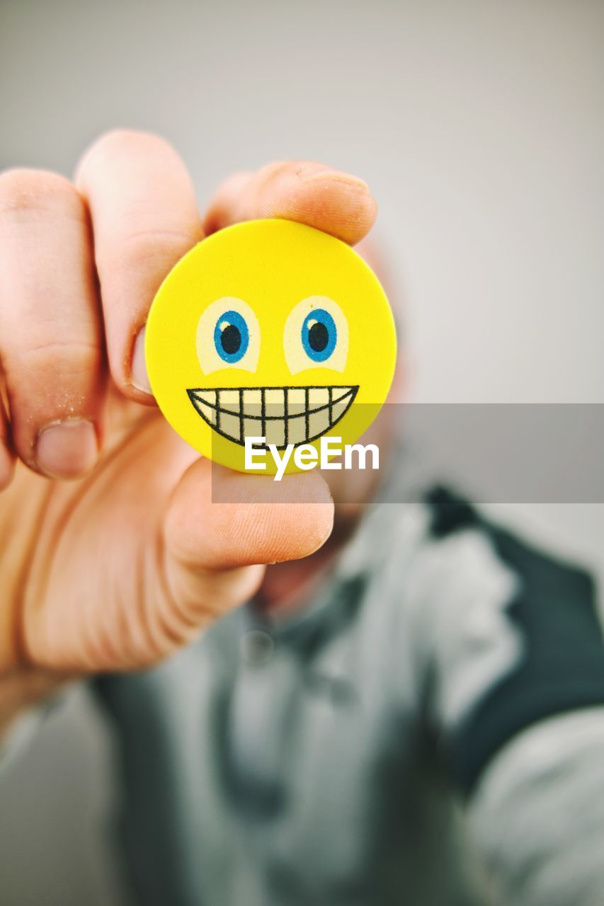 Hand holding yellow happy smiley emoji in front of face