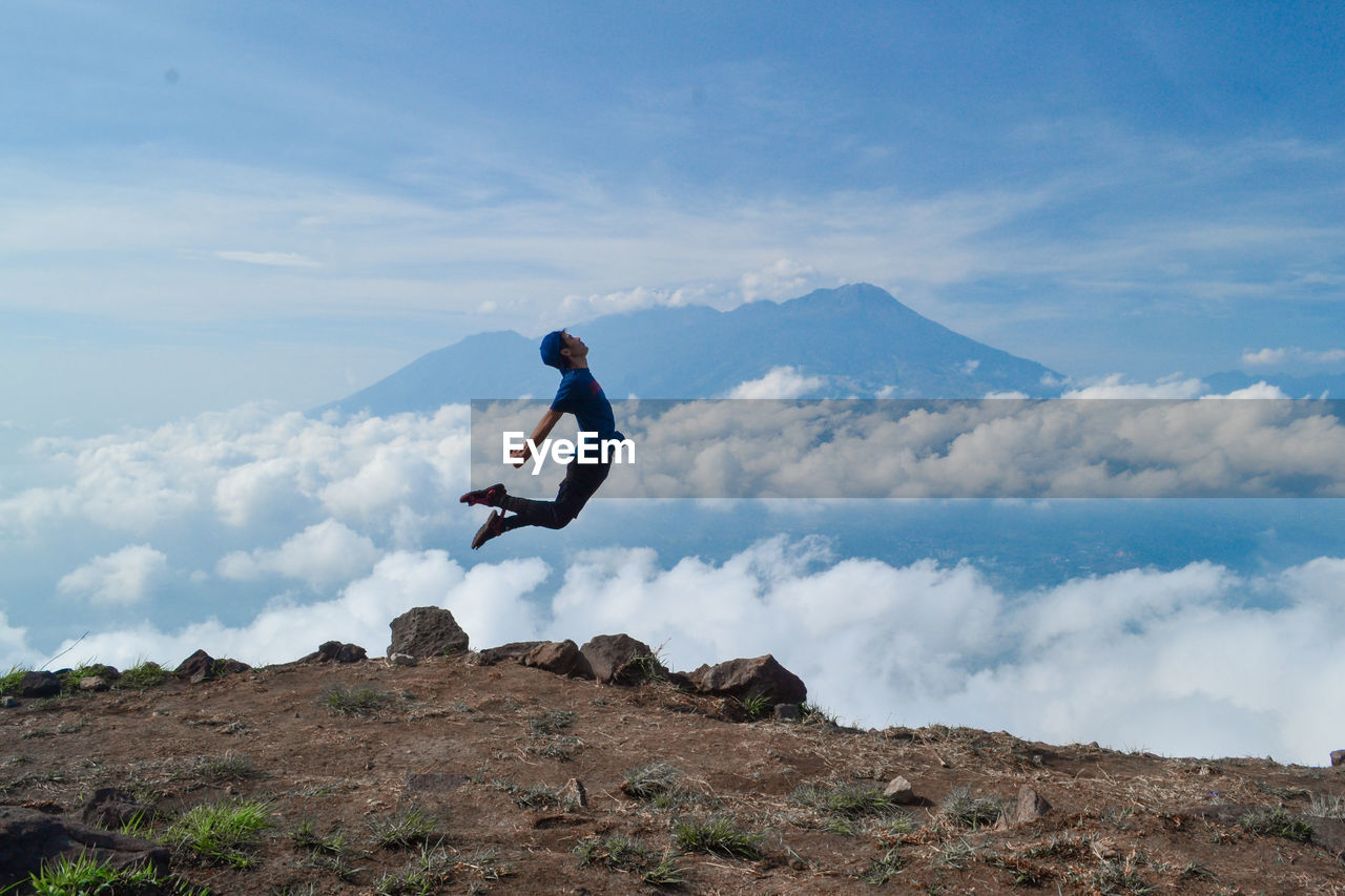 Hiker jumping on mountain peak against sky