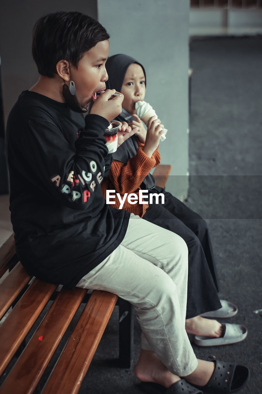 Portrait of young girl and boy licking ice cream while sitting on chair