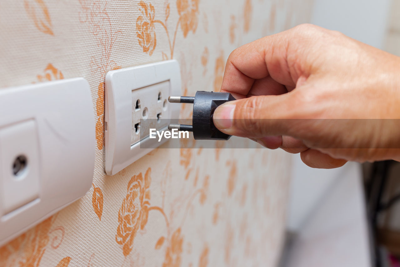 Cropped hand of person putting cable in electric plug