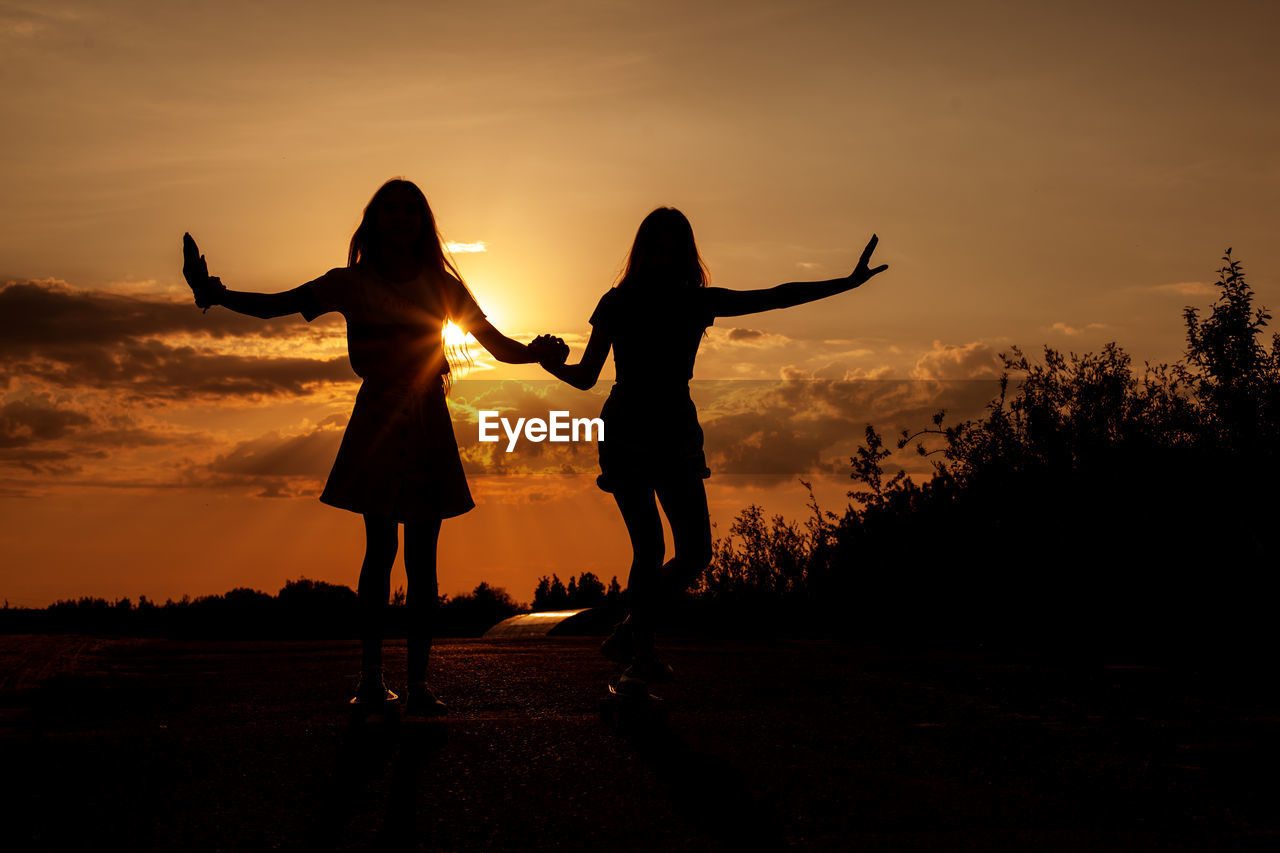 Silhouette friends holding hands standing on land against sky during sunset