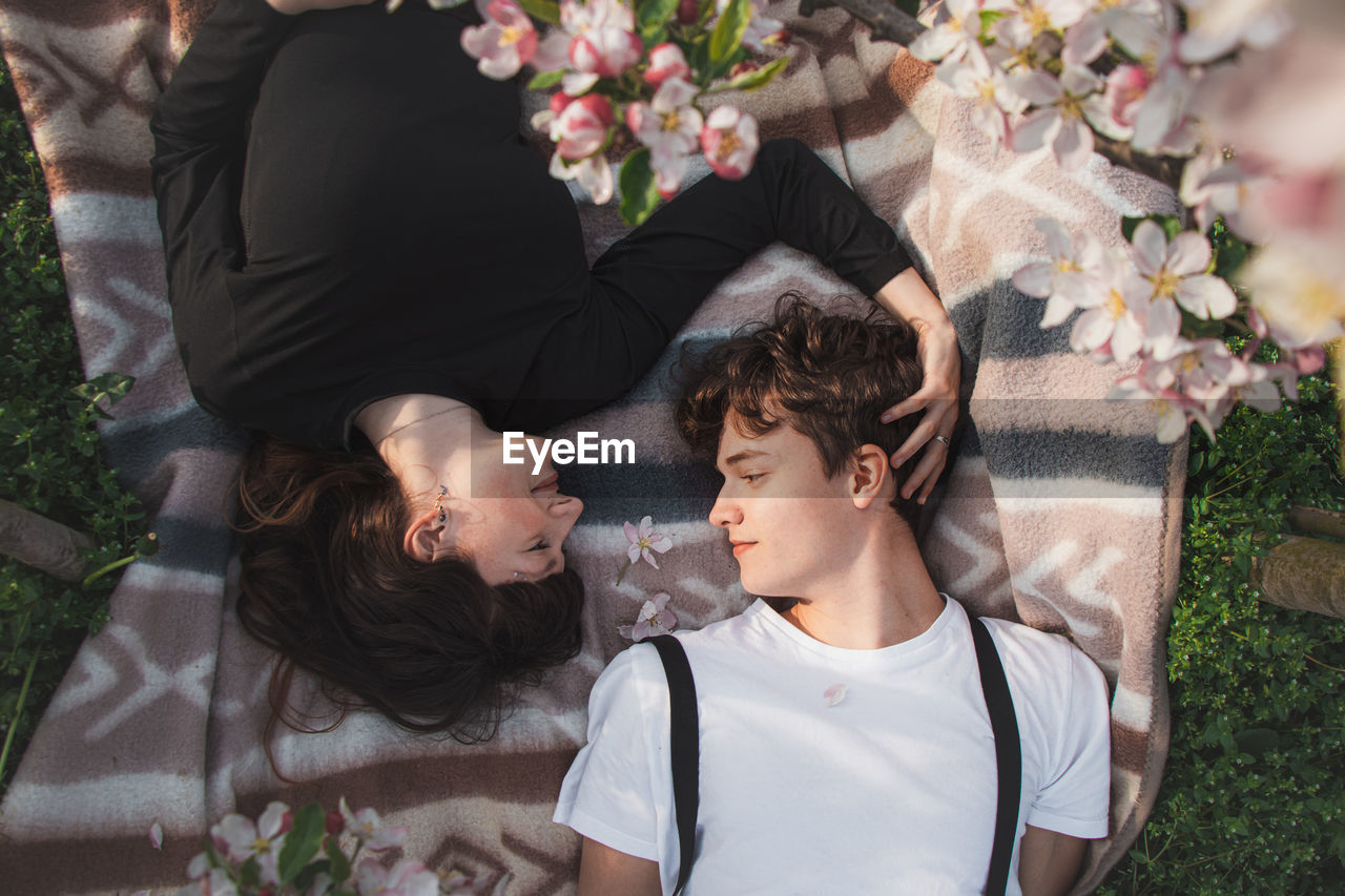 Strong love between two young people lying on a blanket under apple trees. candid portrait of couple