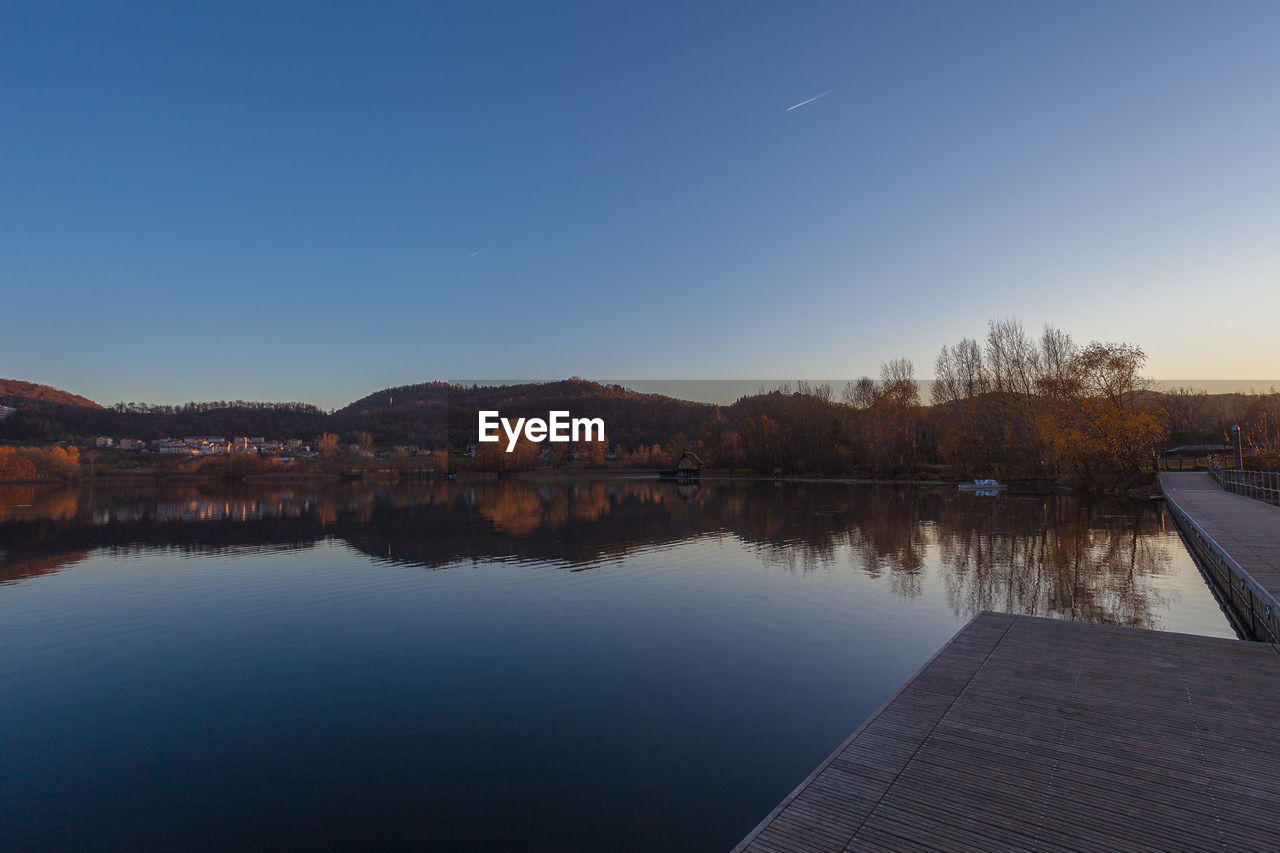 Sunset on hills reflected in the waters of lake with a hut on its banks and boat