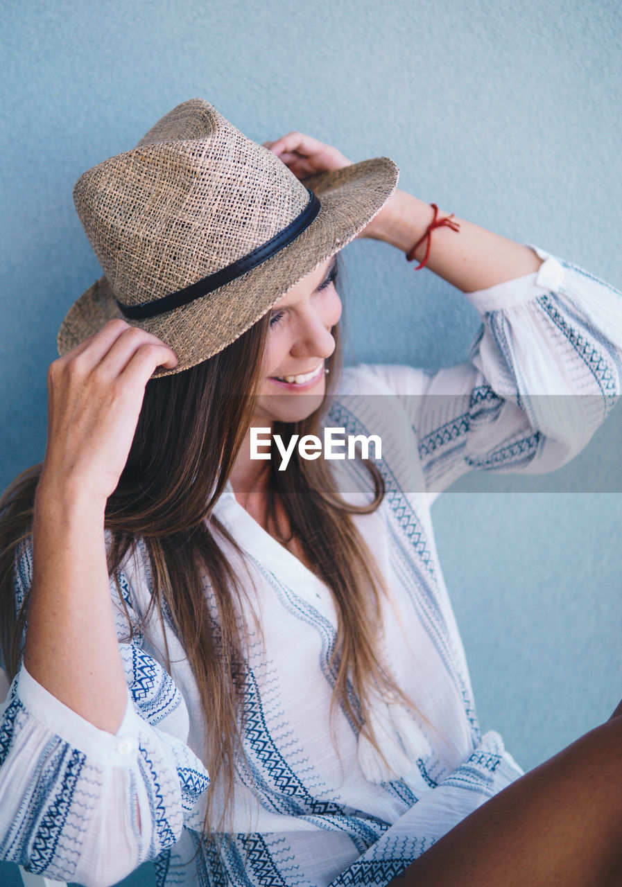 Woman wearing hat sitting on chair against wall