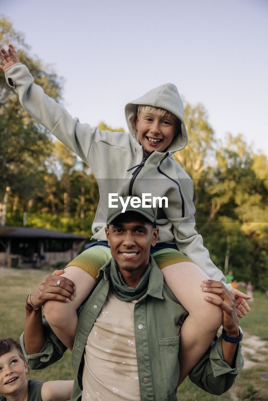 Portrait of male counselor carrying cheerful boy on shoulders while enjoying in playground