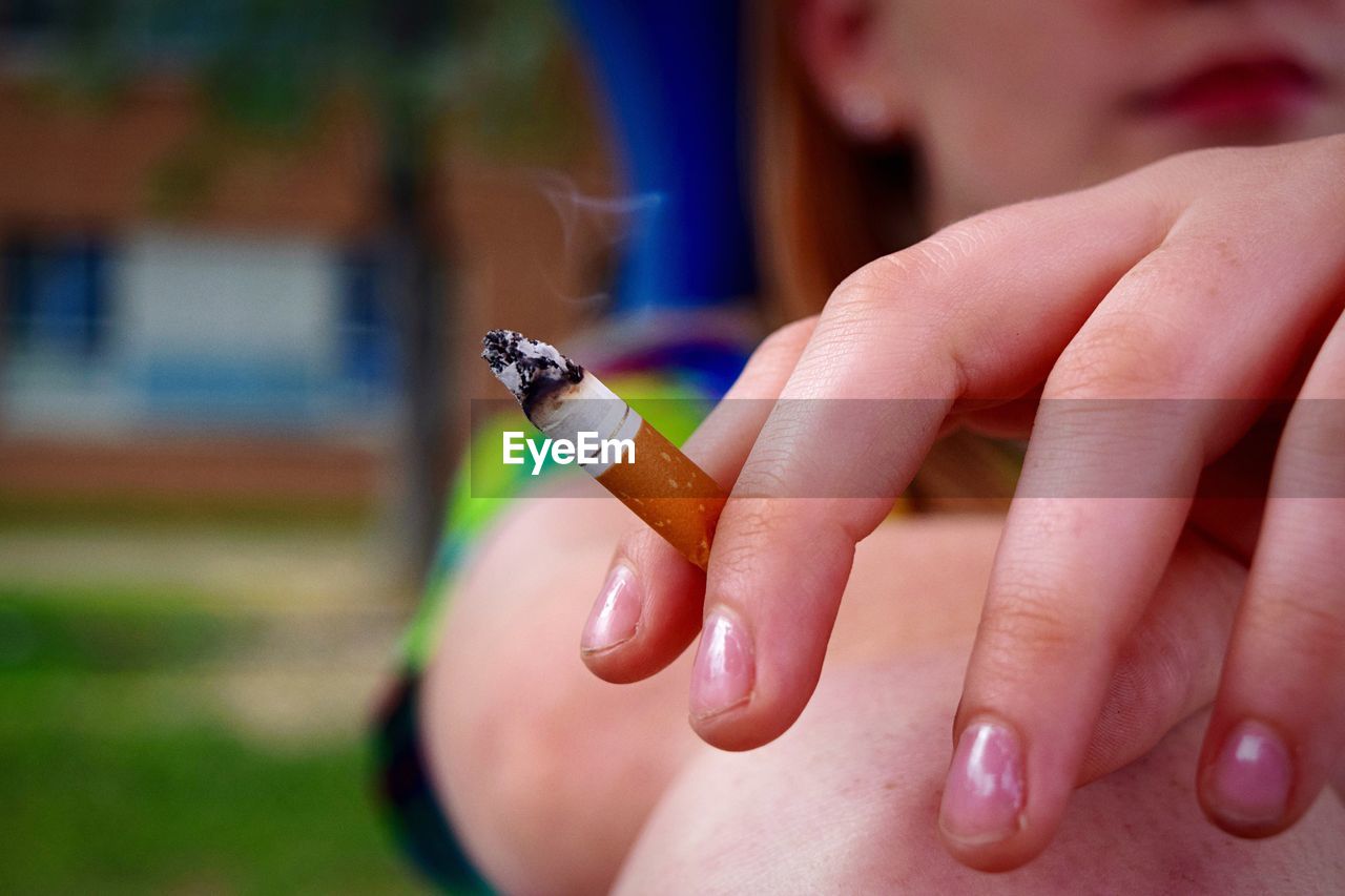 Cropped image of woman hand holding cigarette at park