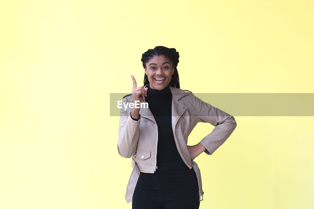 PORTRAIT OF A SMILING YOUNG WOMAN AGAINST YELLOW BACKGROUND