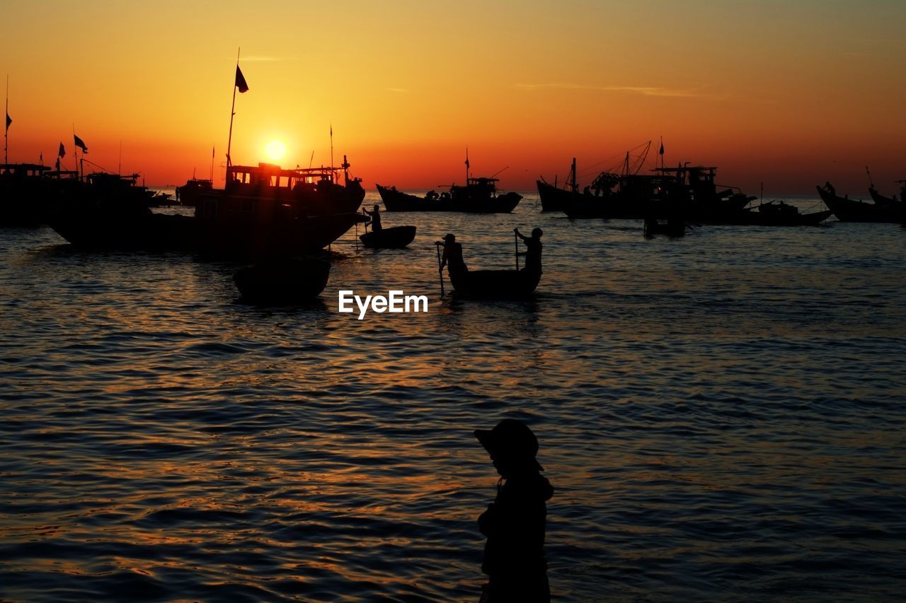 Silhouette people at sea against sky during sunset