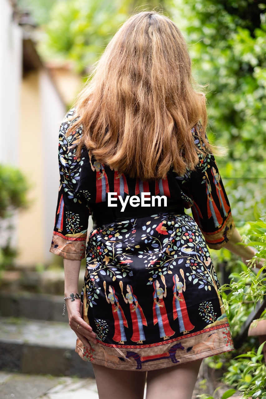 Rear view of woman with blond hair standing by plants at park