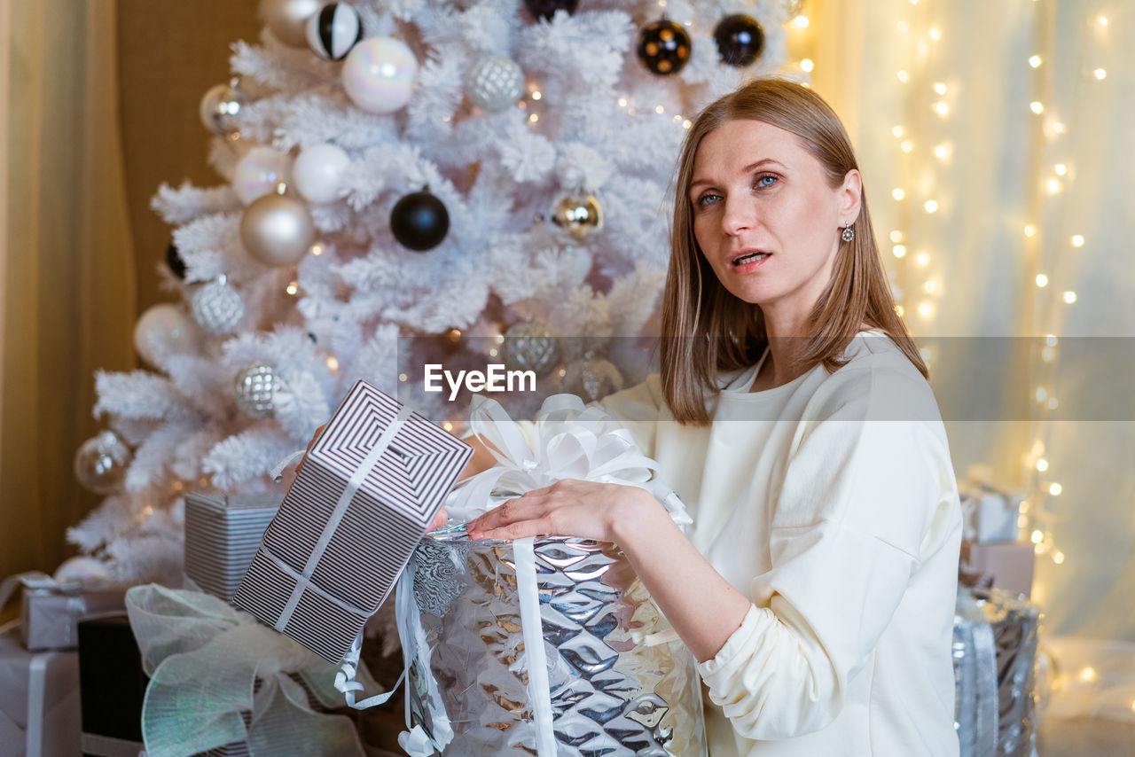 Smiling caucasian young woman opens box with christmas present. christmas