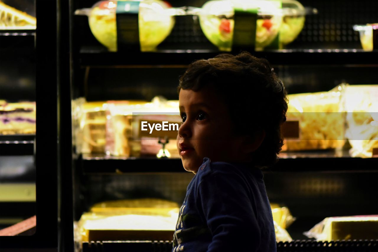 Side view of cute boy looking away against display cabinet in store