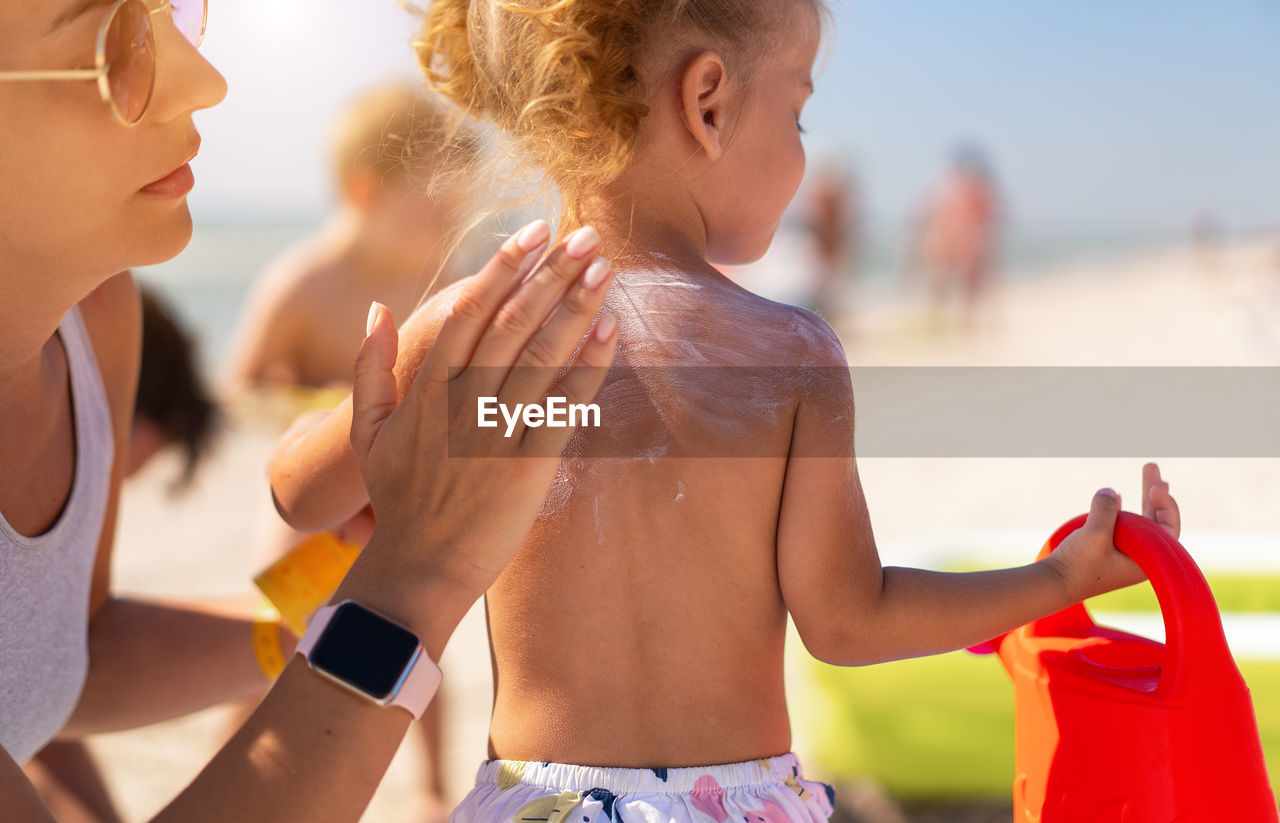 Close-up of mother applying sunscreen on daughter back