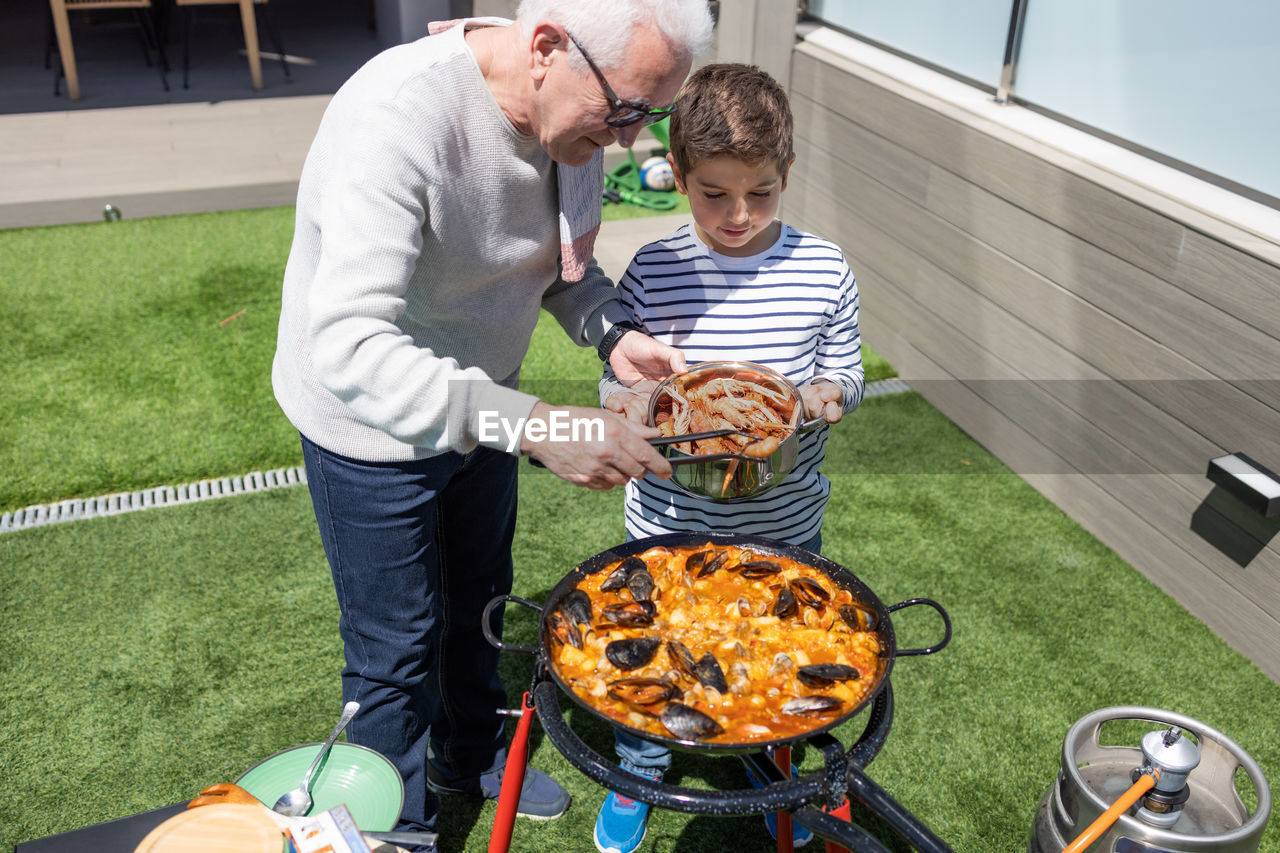 Grandfather and grandson preparing a paella in the garden